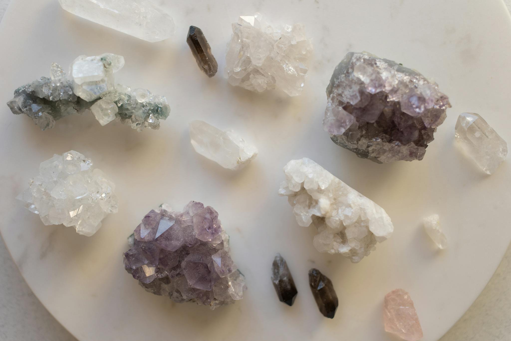 A variety of natural crystals including amethyst and quartz arranged on a white surface.