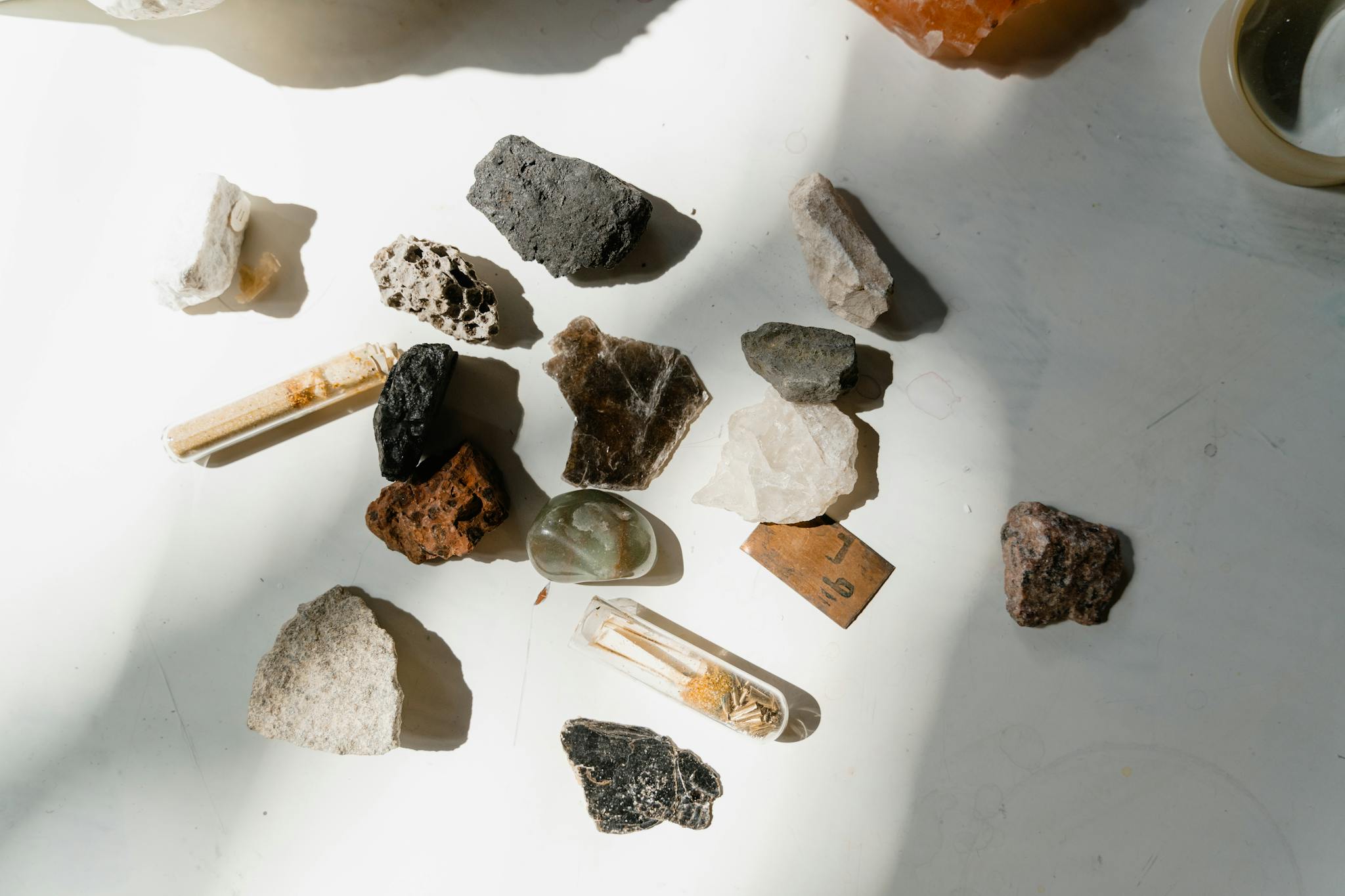 Various minerals and rocks arranged on a sunlit table, showcasing natural textures and colors.